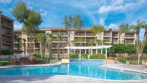 A hotel with a swimming pool, multiple balconies, and a covered area with a pergola.