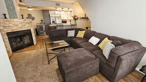 Un salon moderne avec une cheminée en pierre, un canapé d’angle et une table basse en verre.