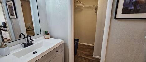 A bathroom with a white vanity, a large mirror, and a shower area visible through a doorway.