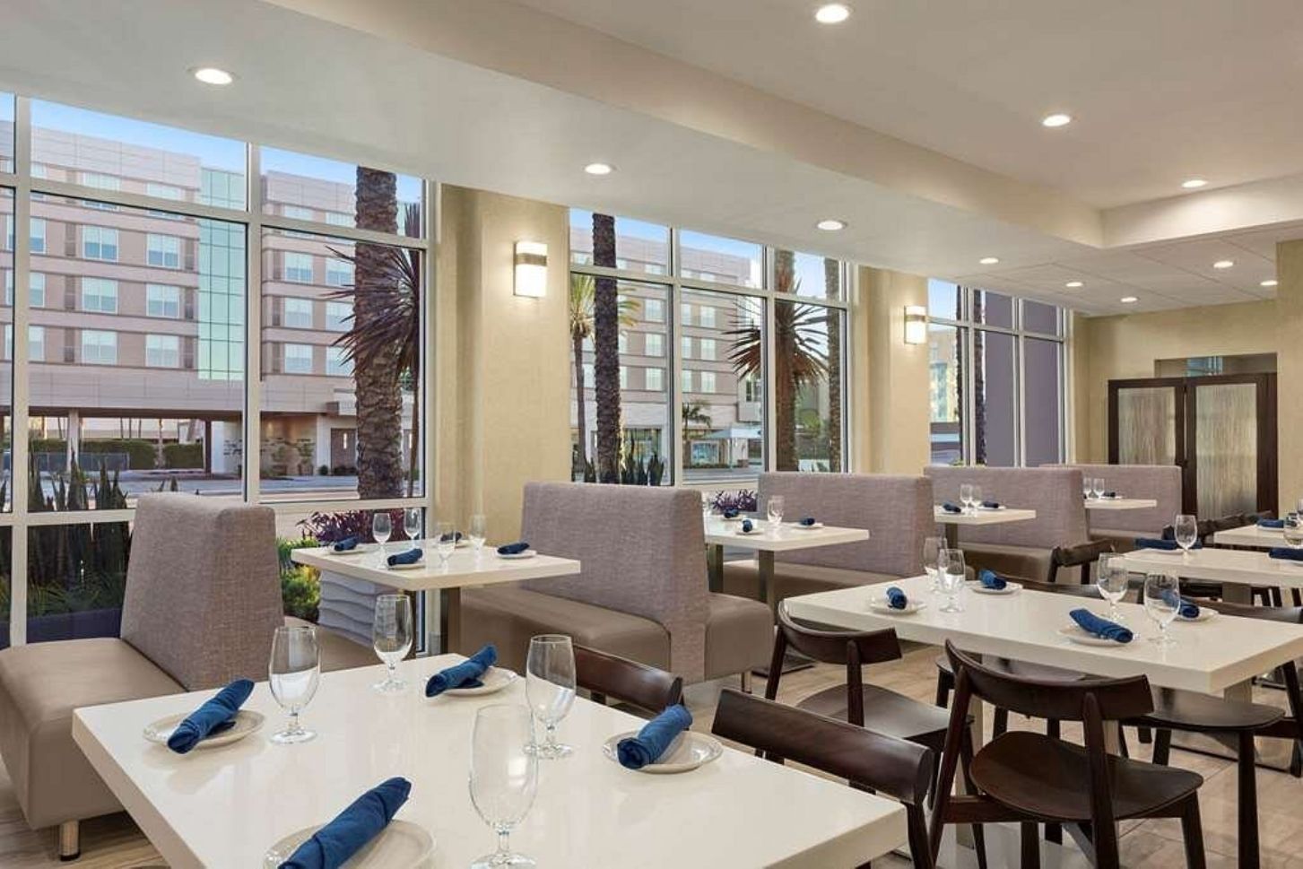 Un restaurant avec des tables et des chaises, de grandes fenêtres et une vue sur les bâtiments environnants.