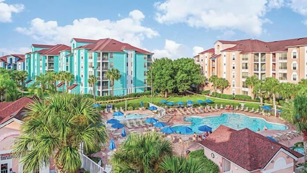 A resort with multiple buildings, a swimming pool, and palm trees.