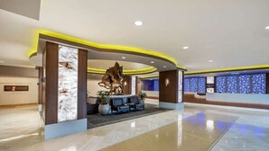 Un moderno vestíbulo de hotel con un mostrador de recepción, zona de estar y paneles decorativos en la pared.