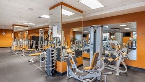 Un gimnasio con diversas máquinas de ejercicio, espejos y paredes anaranjadas.