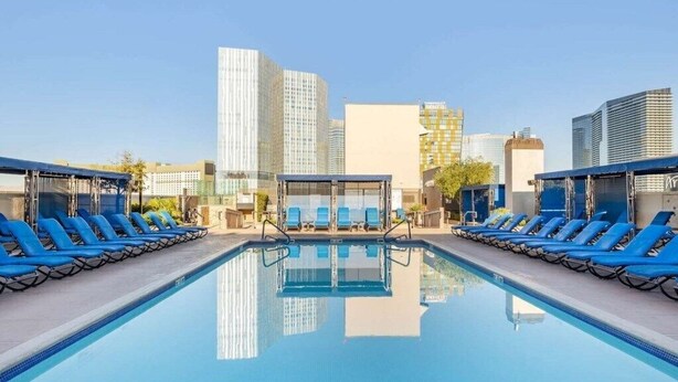 Una piscina en la azotea con sillones de descanso azules y un cerramiento de vidrio en el centro.