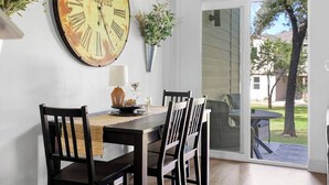 A dining area with a rustic clock, wooden chairs, a table with a placemat, and a view through a sliding glass door to an outdoor patio. - Lakeside Charm at Casa Carmen by the Golf Course (Point Venture)