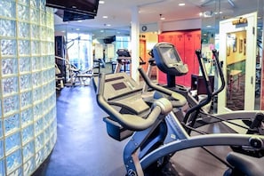 Uma academia com equipamentos de ginástica, parede revestida de azulejos e uma porta vermelha ao fundo.