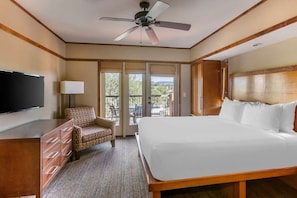 A hotel room with a large bed, a TV, a chair, a desk, and a balcony with a view.