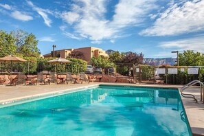 Una piscina con sillas de descanso y sombrillas, rodeada por una valla y árboles.