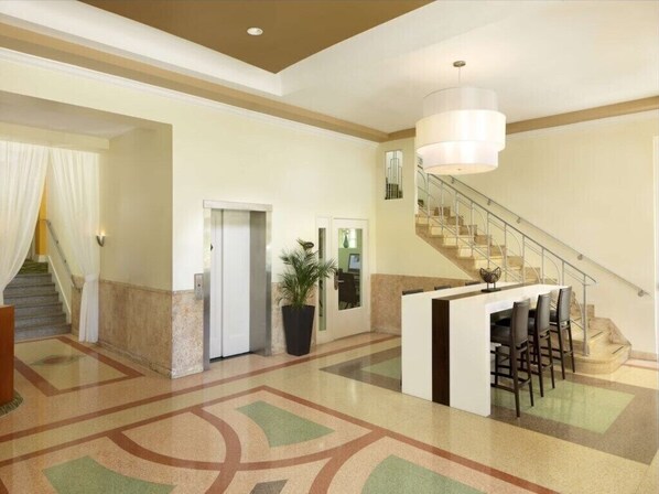 Vestíbulo de hotel con una mesa de recepción, una escalera y una planta en maceta.