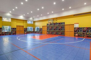 Uma quadra de basquete com piso azul e laranja, cercada por paredes e janelas amarelas.