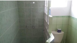 Une salle de bain avec des carreaux verts, des toilettes blanches et une fenêtre.