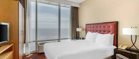 Una habitación de hotel con una cama grande, televisión, escritorio y vista al mar.