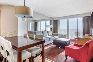 Habitación de hotel con una mesa de comedor, un sofá, un sillón rojo y un ventanal con vistas.