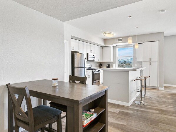 A modern kitchen with white cabinetry, stainless steel appliances, and a wooden dining table with chairs.