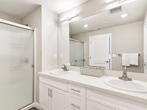 A bathroom with two sinks, a large mirror, a shower, and a towel rack.