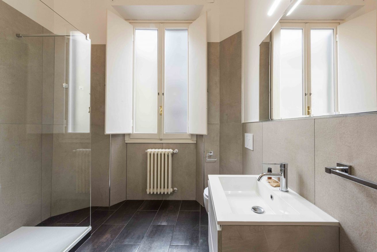 Ein modernes Badezimmer mit einer Duschkabine aus Glas, einem weißen Waschbecken und einem großen Spiegel.