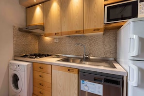 Una cocina compacta con armarios de madera, microondas, lavavajillas, lavadora y salpicadero de azulejos.