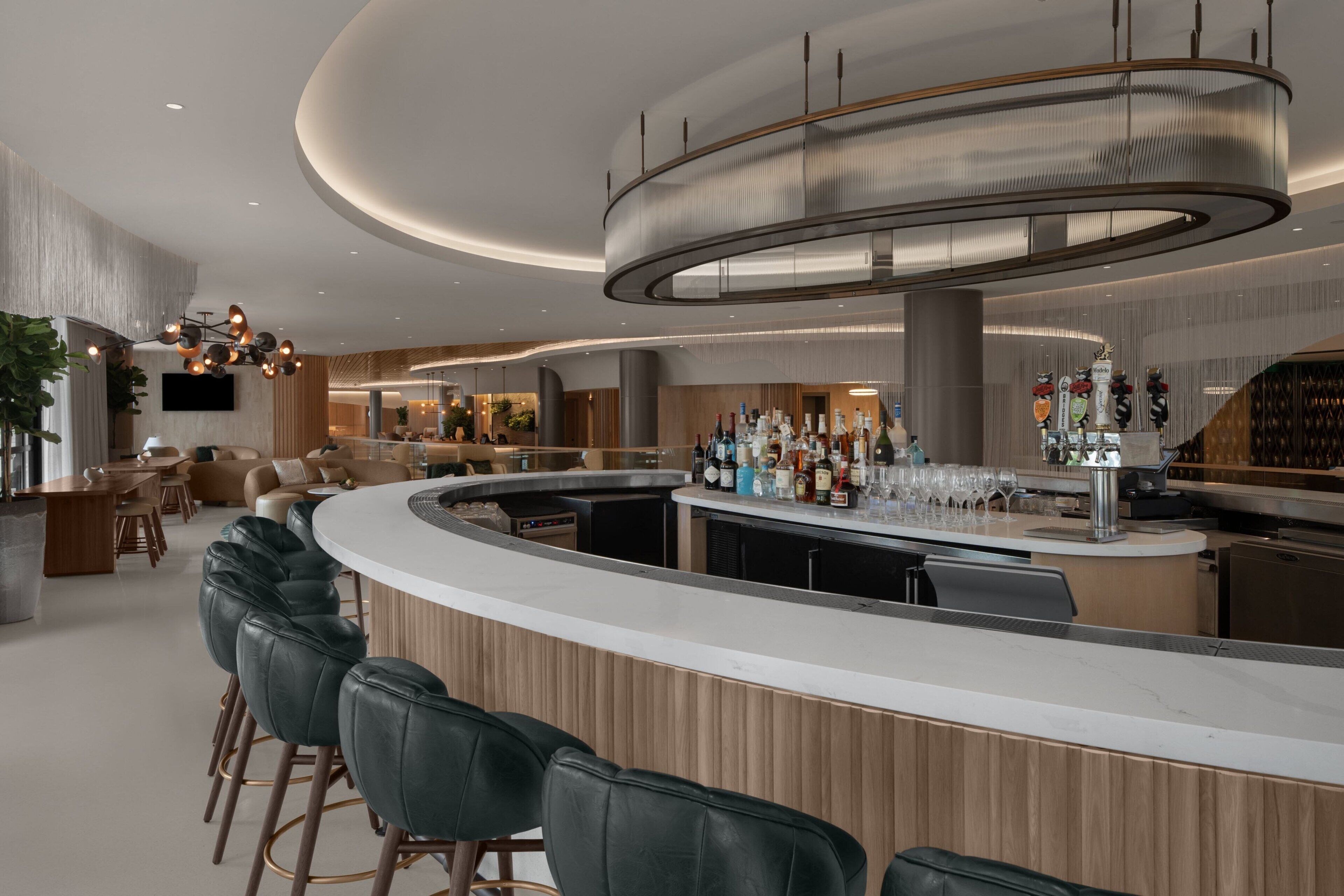 A modern bar area with a curved counter, leather bar stools, and a variety of bottles and glasses.