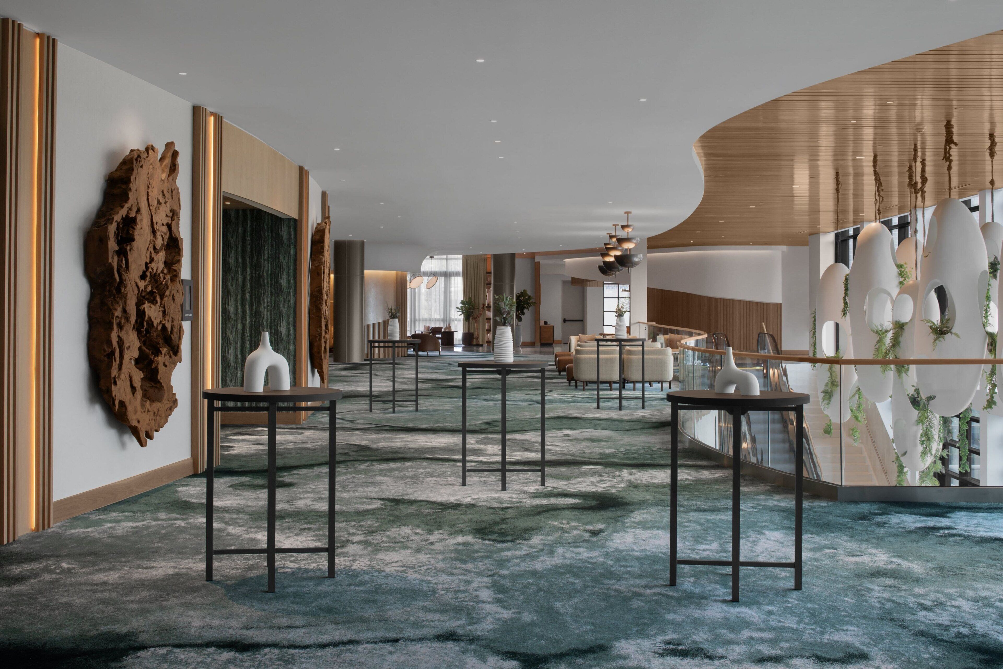 A spacious lobby with a modern design, featuring a large wooden sculpture, a marble wall, and a unique ceiling structure.