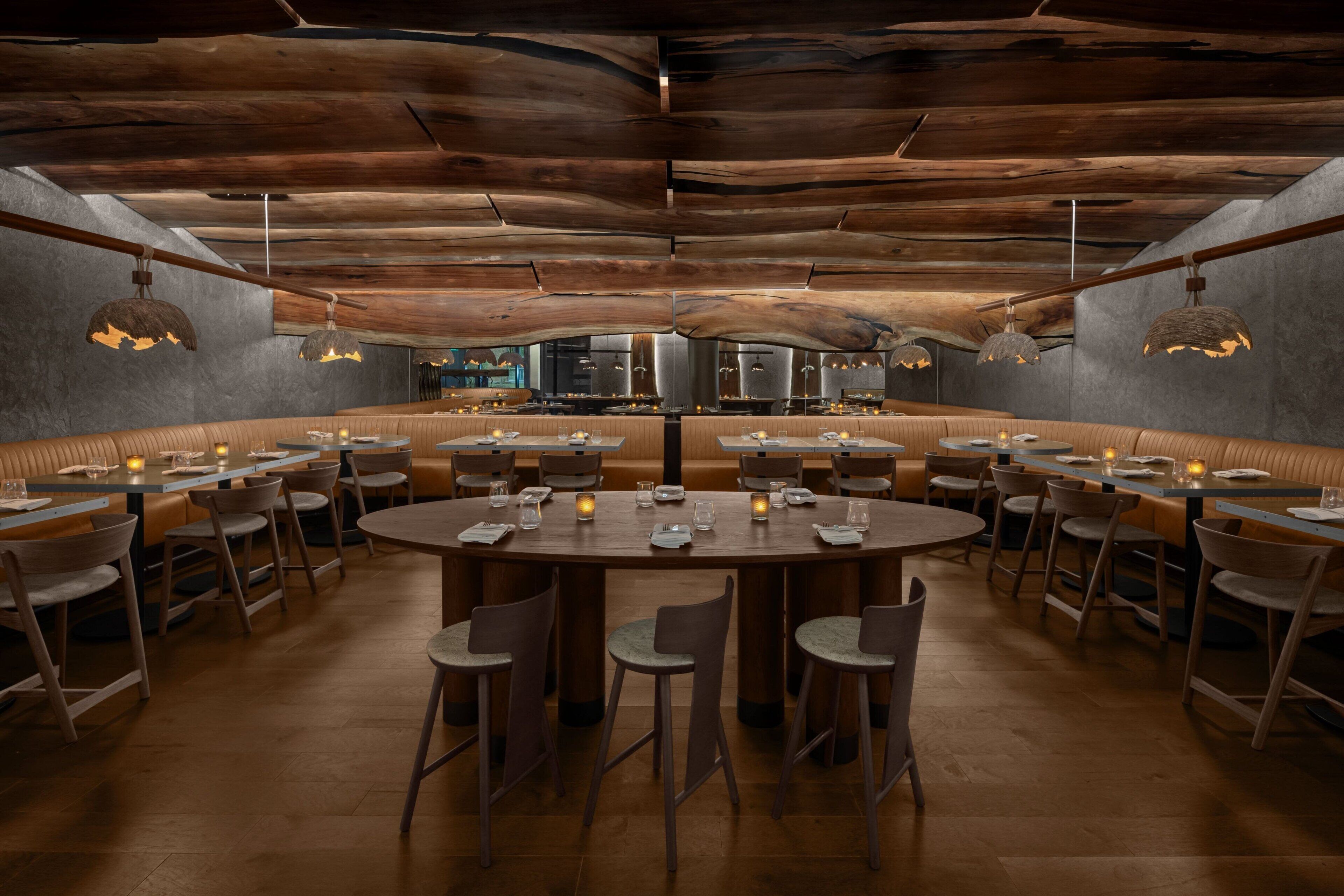 A restaurant with round tables and booths, wooden ceiling, and pendant lighting.