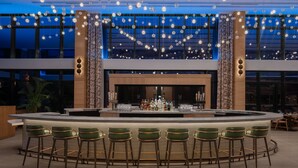 Eine moderne Bar mit einer zentralen Theke, Barhocker und Pendelleuchten.