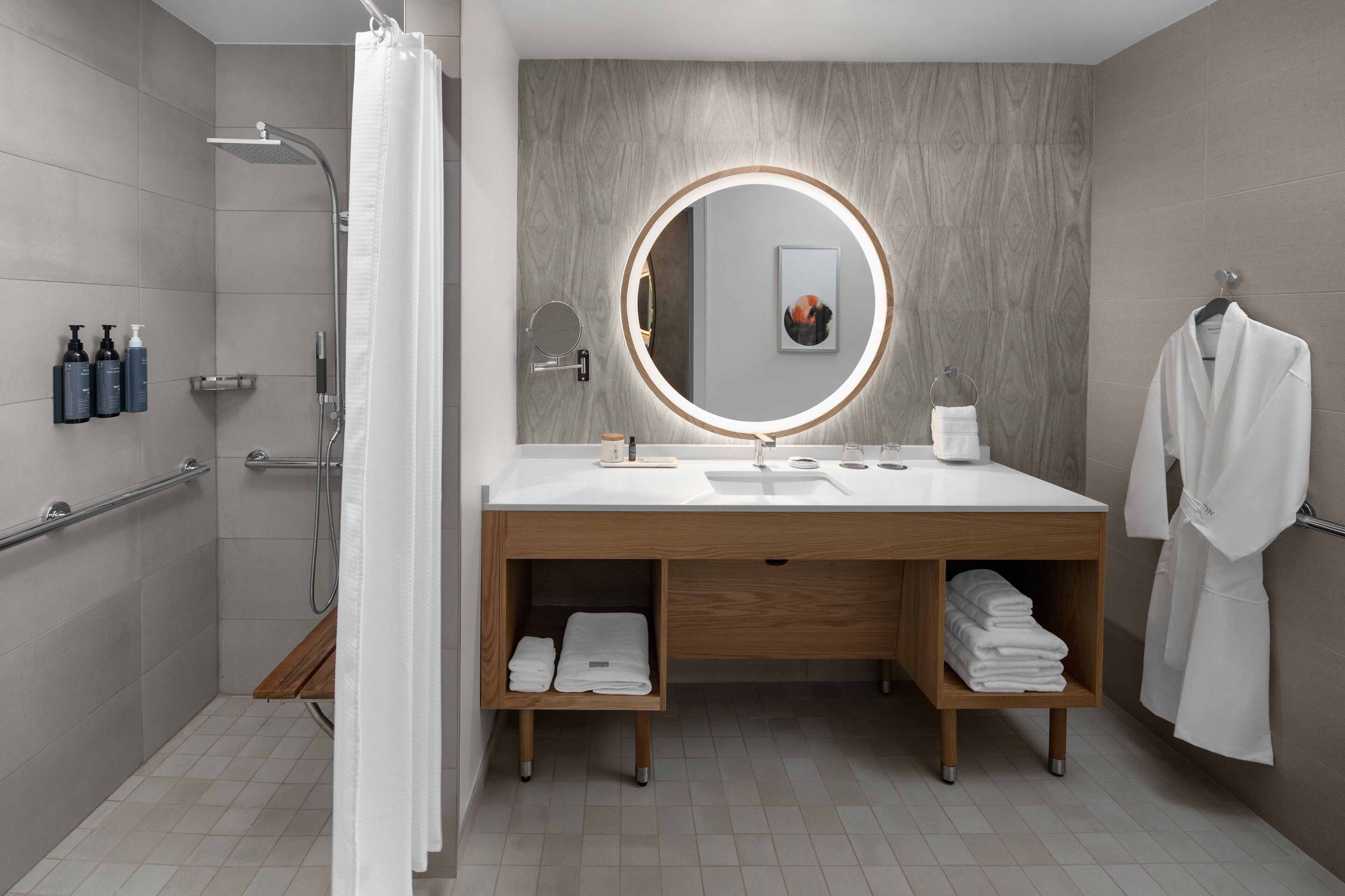 Un baño moderno con ducha, un lavabo con espejo y una bata colgada en la pared.