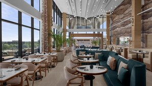 Ein modernes Restaurant mit hohen Decken, großen Fenstern und einer Mischung aus Sitzgelegenheiten, darunter Tische und Sofas.