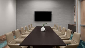 A conference room with a long table, beige chairs, a flat-screen TV on the wall, and a vase with a plant.