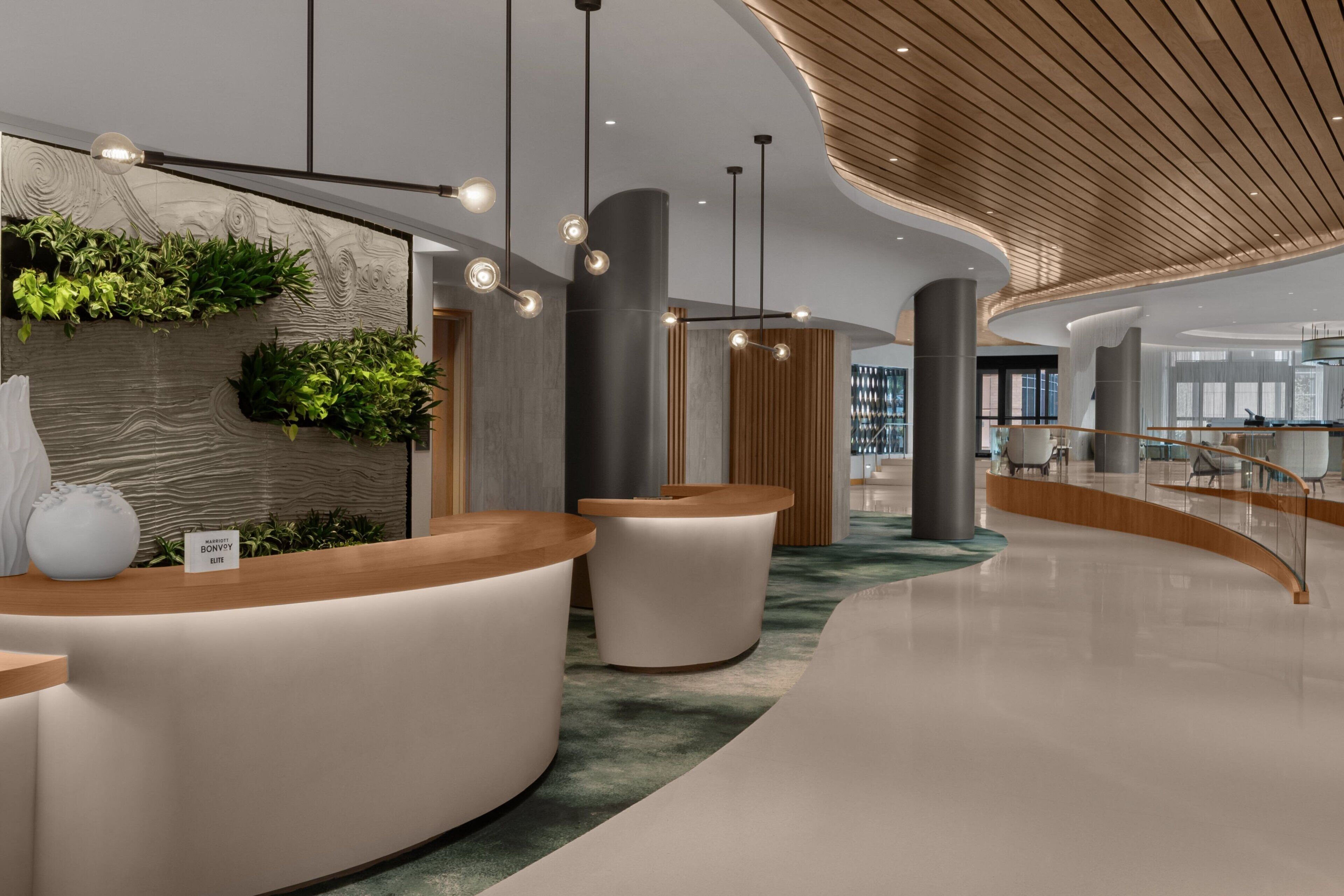 Un área de recepción moderna con un mostrador curvo, un jardín vertical en la pared y un techo de madera.