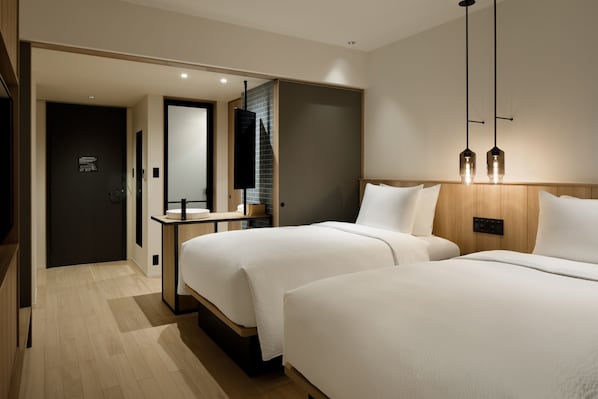 Una habitación de hotel moderna con dos camas, cabecero de madera, mesita de noche, espejo y lámpara colgante.