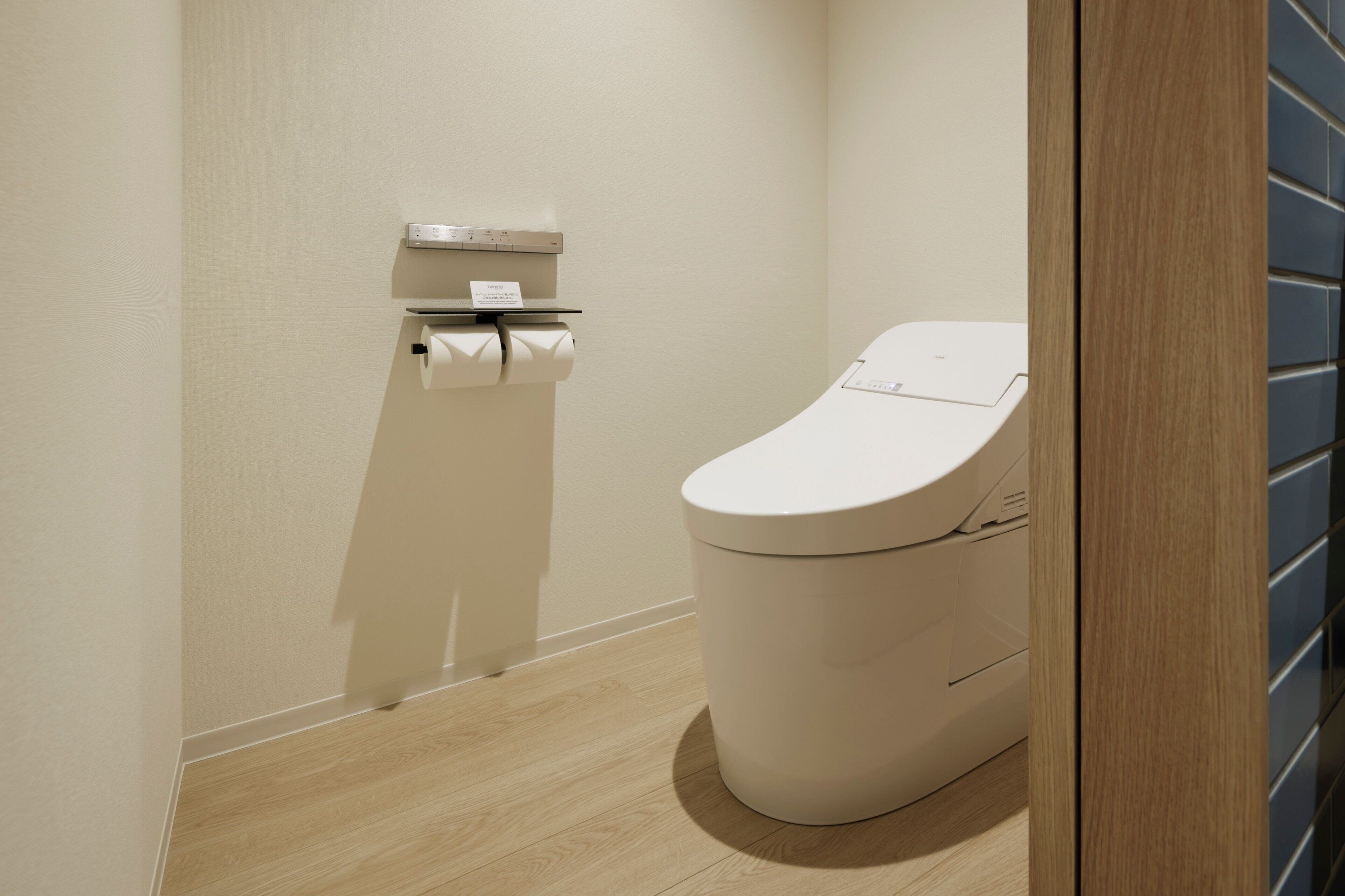 Un baño moderno con inodoro, dispensador de toallas de papel y mecanismo para tirar de la cisterna.