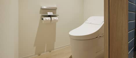 A modern bathroom with a toilet, a paper towel dispenser, and a flush handle.