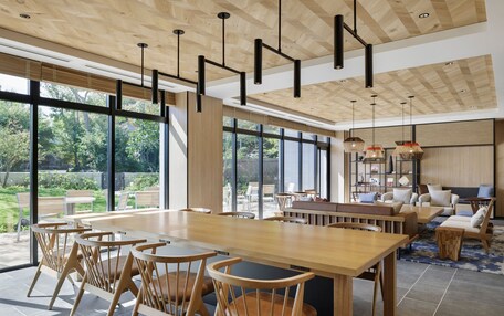 A spacious dining area with a long wooden table and chairs, large windows offering a view of the outdoors, and a cozy seating area with sofas and a coffee table.