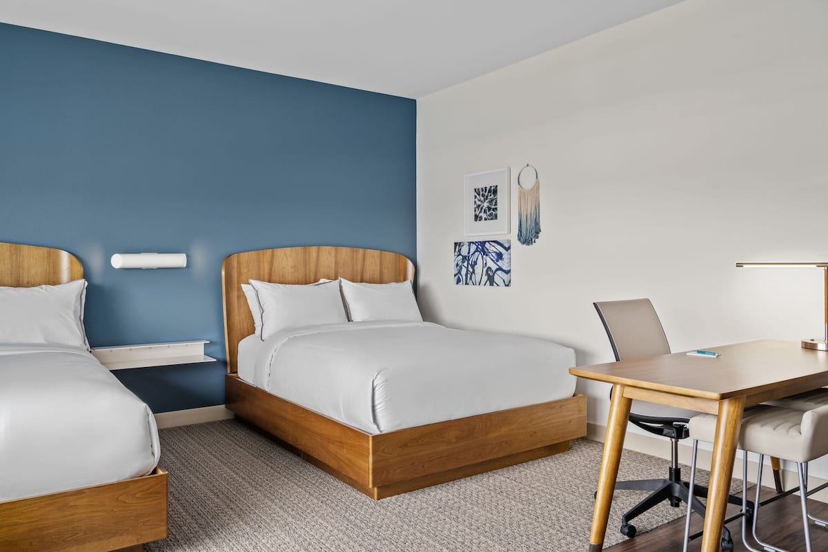 A hotel room with two beds, a desk, and a chair.