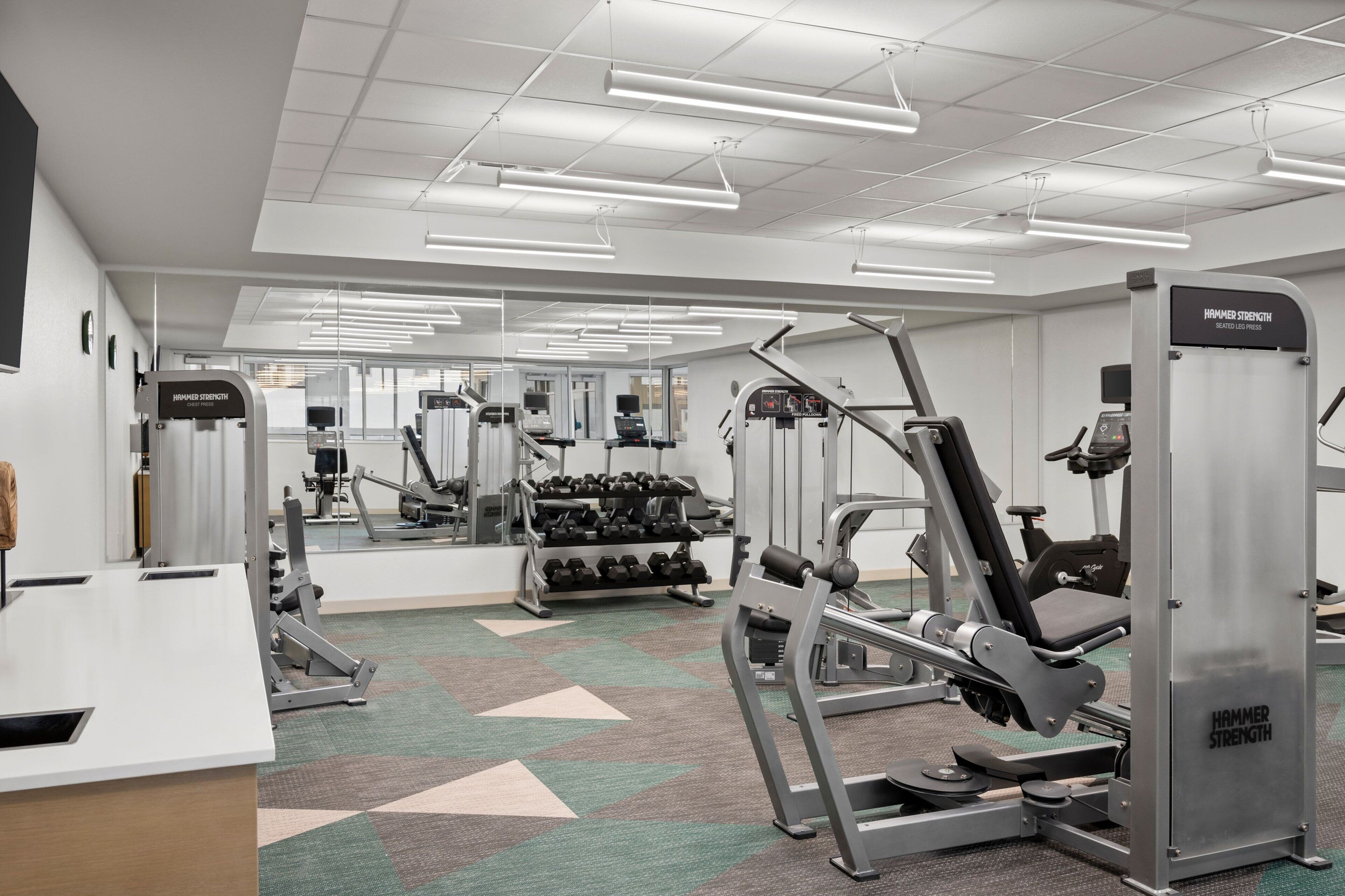 A gym with various exercise equipment, including a Hammer Strength machine, and a mirrored wall.