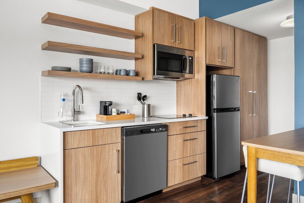 A modern kitchen with wooden cabinets, a stainless steel refrigerator, a microwave, and a dishwasher.