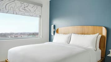 Une chambre d’hôtel avec un grand lit, une fenêtre donnant sur un beau paysage et un mur bleu.