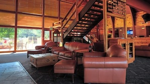 A spacious interior with leather sofas, a wooden staircase, and large windows. - Payson | Secluded Cabin Retreat | Pool + Hot Tub (Payson)