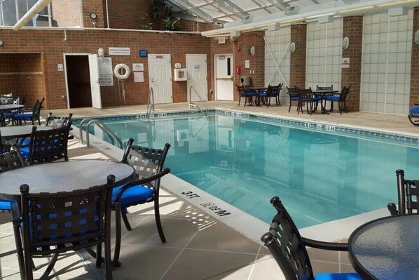 Una piscina interior con agua cristalina, rodeada de mesas y sillas.