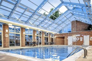 Una piscina interior con techo de cristal, paredes de ladrillo y zona de estar.