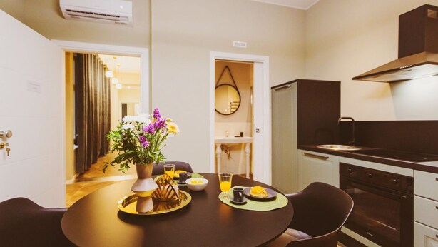 A modern kitchen with a stove, oven, and a dining area with a table set for two. - GuestHost - Chiara Comfy Apartment D (Udine)