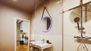 A bathroom with a white sink, a round mirror, a shower, and a wooden floor.