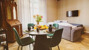 A room with a dining table set for breakfast, a bed, a TV mounted on the wall, and a wooden dresser.