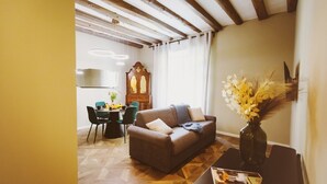 A living room with a sofa, a dining table with chairs, a wooden floor, and a wall-mounted clock.