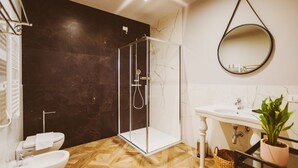 Un baño con ducha envuelta en vidrio, un lavamanos blanco, un espejo y una planta en maceta.