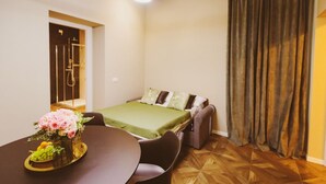Habitación de hotel con cama, una mesa de comedor con sillas, zona de ducha y un ventanal con cortinas.