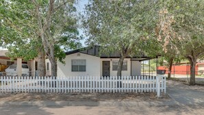 A single-story house with a white exterior, a small porch, and a white picket fence. - Modern Home in Edinburg: Half-Mi Walk to UTRGV! (Edinburg)