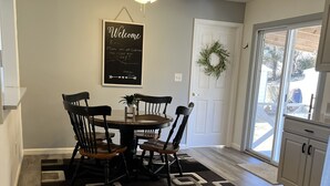Un coin repas avec une table ronde, quatre chaises, un ventilateur de plafond et un panneau d’accueil.