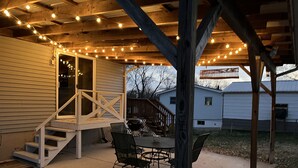 Une terrasse couverte avec une table et des chaises, un barbecue et des guirlandes lumineuses.