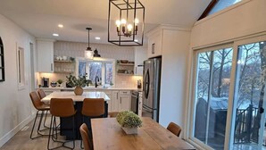 A modern kitchen with a central island, a dining area with a wooden table and chairs, and large windows offering a view of the outdoors. - Island View McDonald Lake (Dent)
